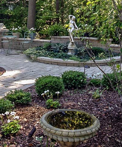 moonlight garden shown without all white floowers and with unilock brussels patio and seat wall with landscape lighting and statue in Flint, MI