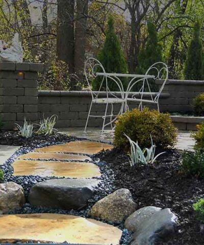 moonlight garden shown after rain with deerskin large flagstone walk to unilock brussels patio and seat wall with landscape lighting and statue in Flint, MI