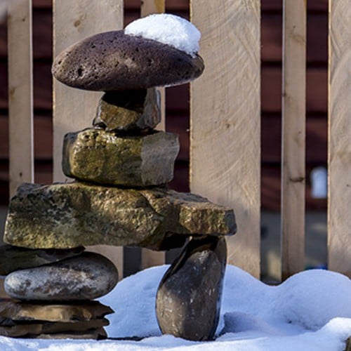 Stacked Stone figure in front of custom cedar fence shown in snow in winter with a snow cap